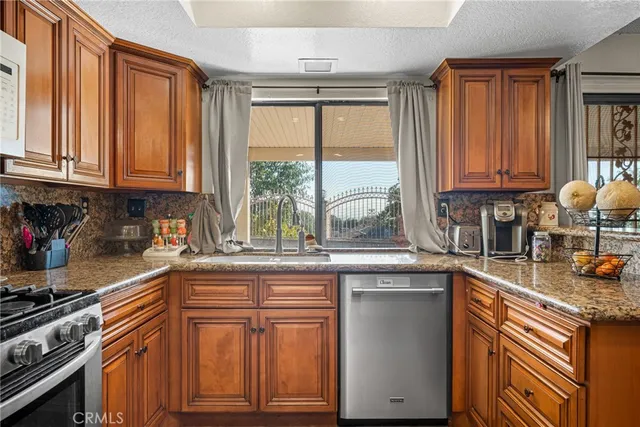 a kitchen with granite countertop wooden cabinets a sink and a stove next to a window