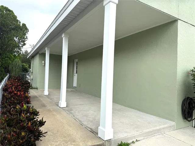 a view of a white house in front of a big yard with plants and large trees