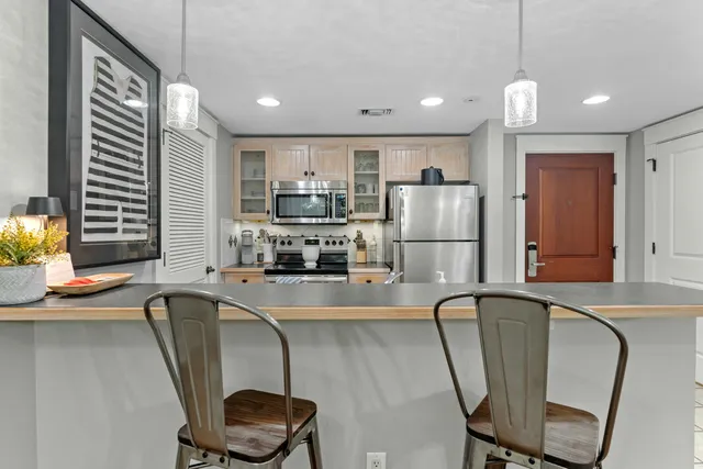 a kitchen with stainless steel appliances granite countertop a dining table chairs refrigerator and sink