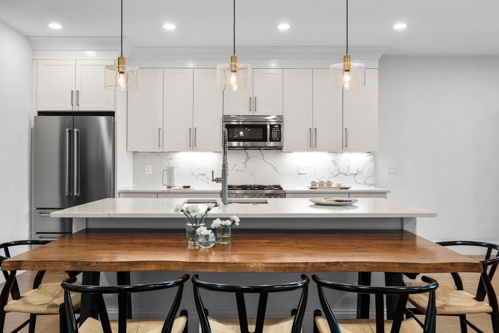 258-260 West 3rd Street, Unit 1 Boston, MA 02127 - Photo 13 of 37 a kitchen with stainless steel appliances granite countertop a stove a refrigerator and a dining table with wooden floor