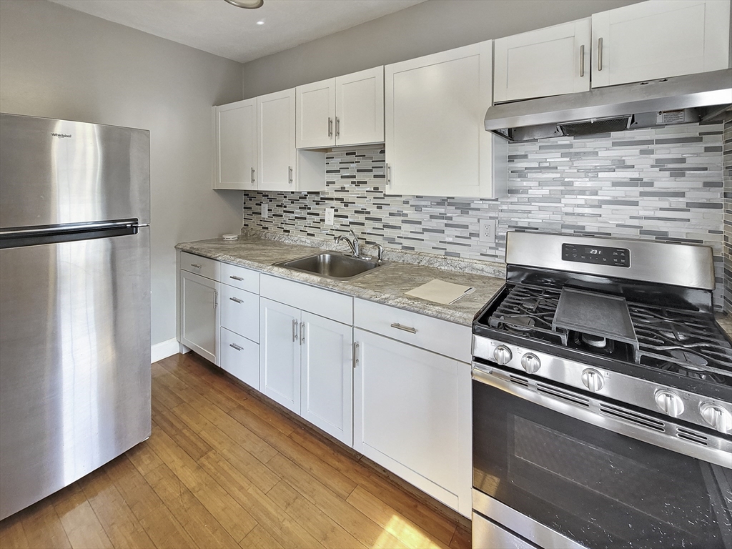 338-342 Warren Street, Unit 6 Boston, MA 02119 - Photo 3 of 7 a kitchen with cabinets stainless steel appliances and wooden floor