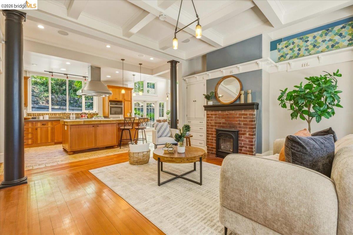 1631 La Vereda Road Berkeley, CA 94709 - Photo 5 of 42 Open-concept living space featuring wood-finish flooring, a brick fireplace with an insert, a wood-finish kitchen island, exposed ceiling beams, and integrated recessed lighting