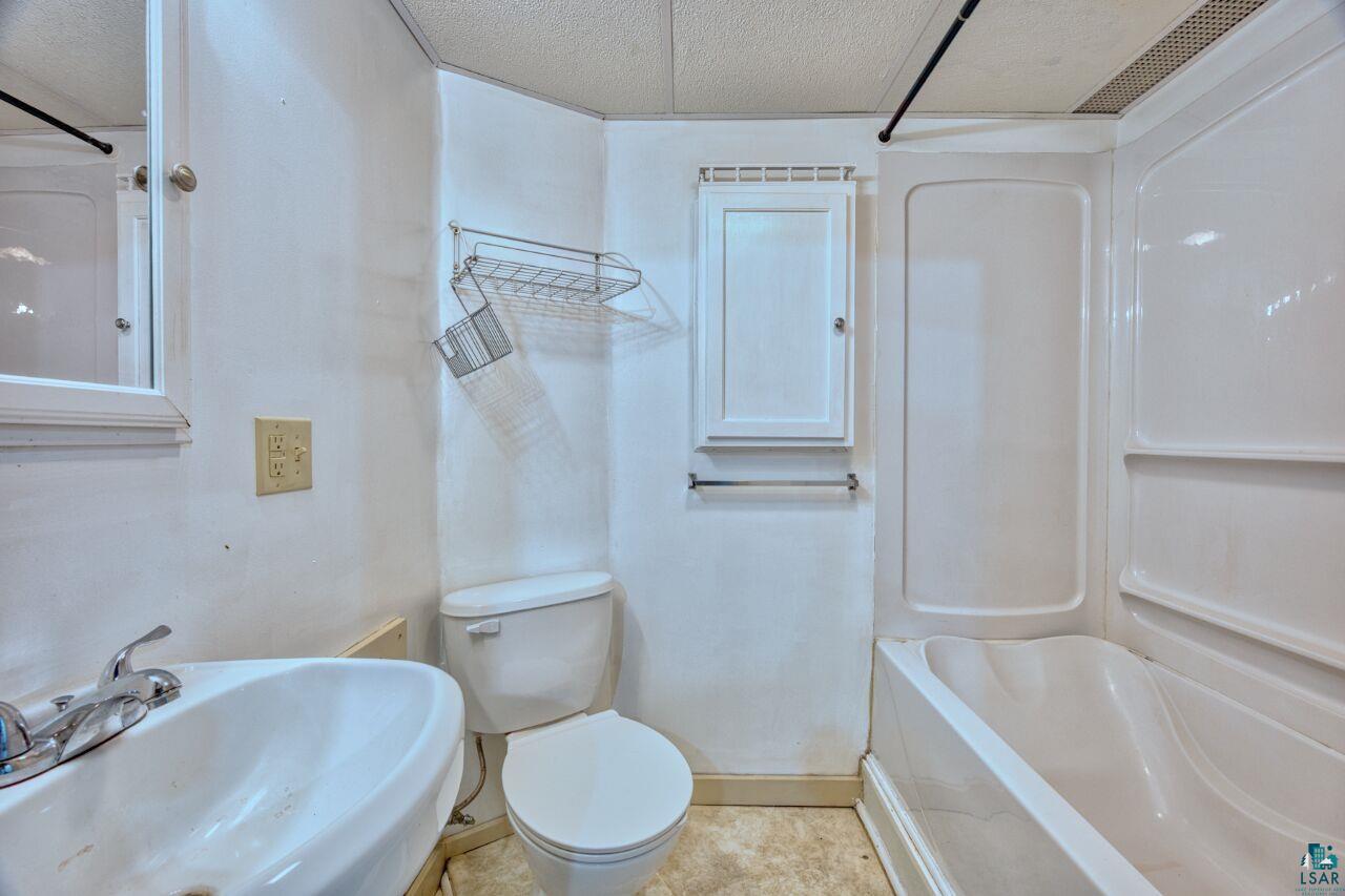 4191 Kerr Location Hibbing, MN 55746 - Photo 19 of 37 Full bathroom with a sink, a textured ceiling, baseboards, toilet, and tub / shower combination