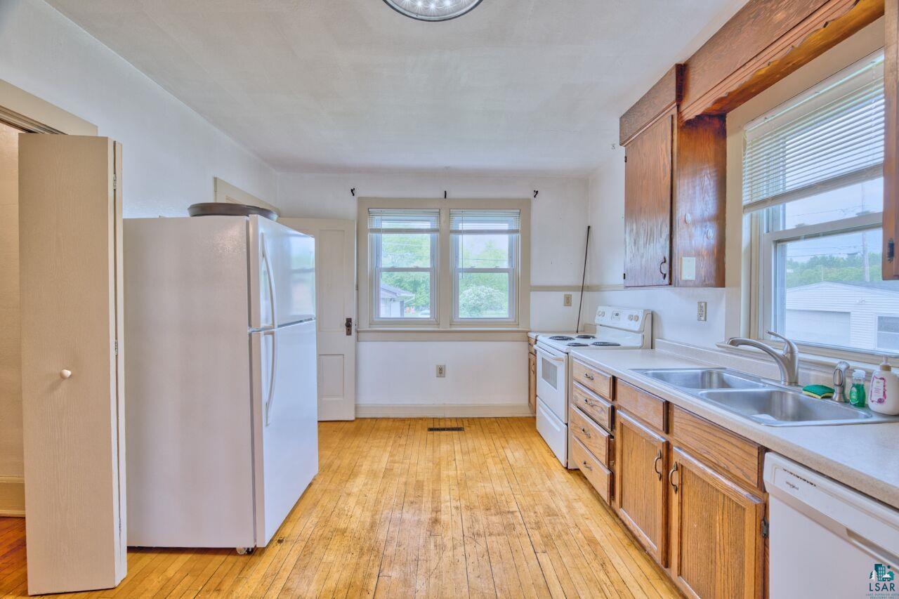 4191 Kerr Location Hibbing, MN 55746 - Photo 6 of 37 Kitchen with white appliances, a sink, light wood-style floors, light countertops, and brown cabinetry