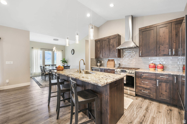 4527 North Seven Bridges Road Eden, UT 84310 - Photo 14 of 65 Kitchen with dark wood finish cabinetry, light stone counters, stainless steel range with gas stovetop, a kitchen breakfast bar, and vaulted ceiling