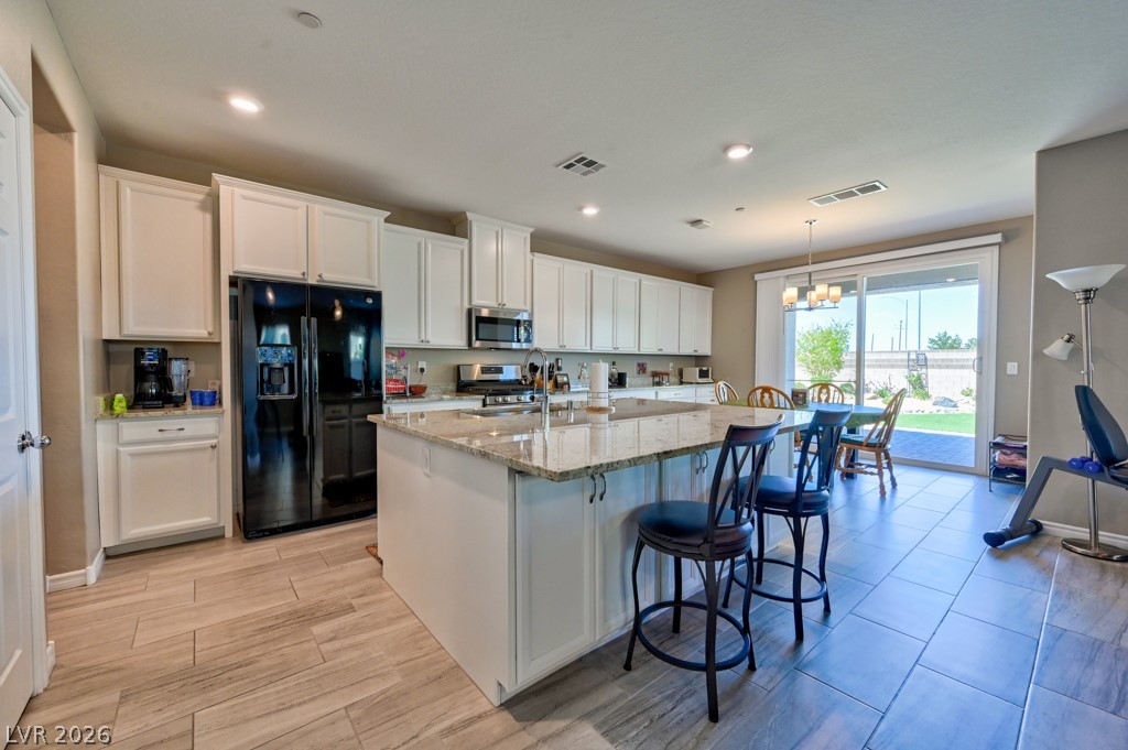 1054 Langston Ranch Avenue Henderson, NV 89002 - Photo 19 of 82 Kitchen featuring light and bright white cabinetry, stainless steel & black appliances, light granite countertops, a huge Chef's island with sink and seating. Modern tile floors. Abundance of cabinetry.