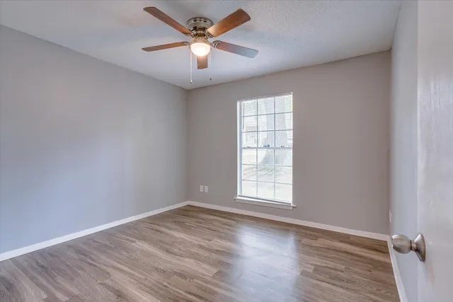 an empty room with wooden floor ceiling fan and windows