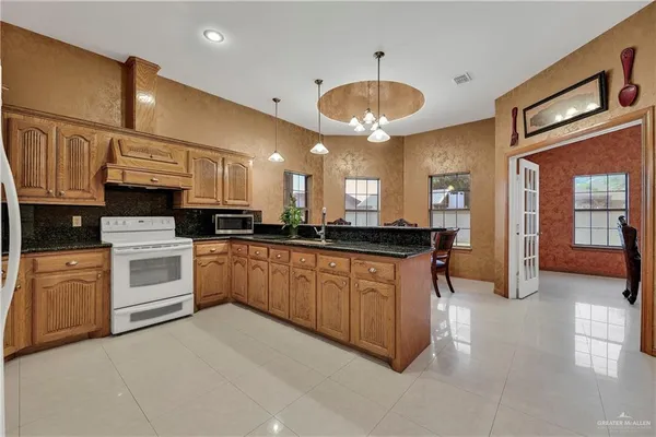 a large white kitchen with stainless steel appliances granite countertop a stove a sink a refrigerator and a microwave