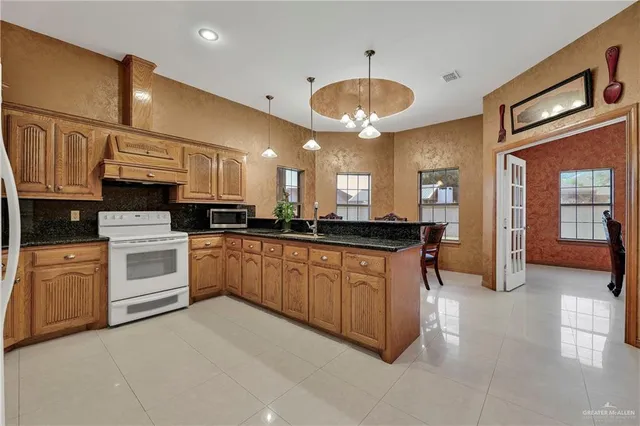 a large white kitchen with stainless steel appliances granite countertop a stove a sink a refrigerator and a microwave
