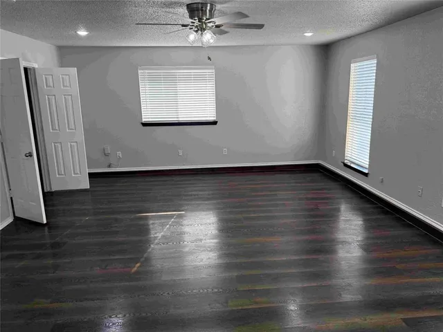 an empty room with wooden floor chandelier fan and windows