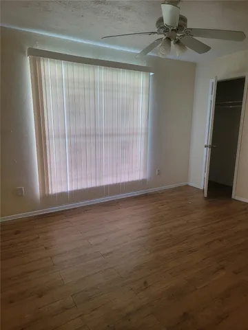 an empty room with wooden floor fan and windows