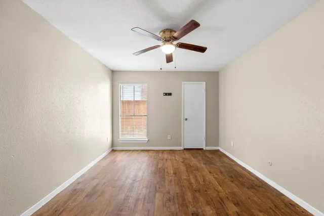 an empty room with wooden floor fan and windows