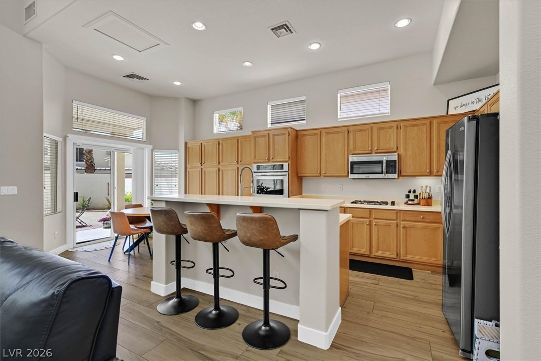 1259 Moon Vision Street Henderson, NV 89052 - Photo 9 of 53 A vibrant kitchen with light wood cabinetry, offering an inviting island and clear sightlines to the outdoor patio.