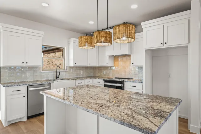 a kitchen with kitchen island granite countertop a sink a stove and white cabinets