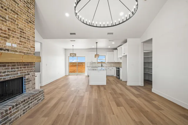 an empty room with wooden floor kitchen view and a fireplace