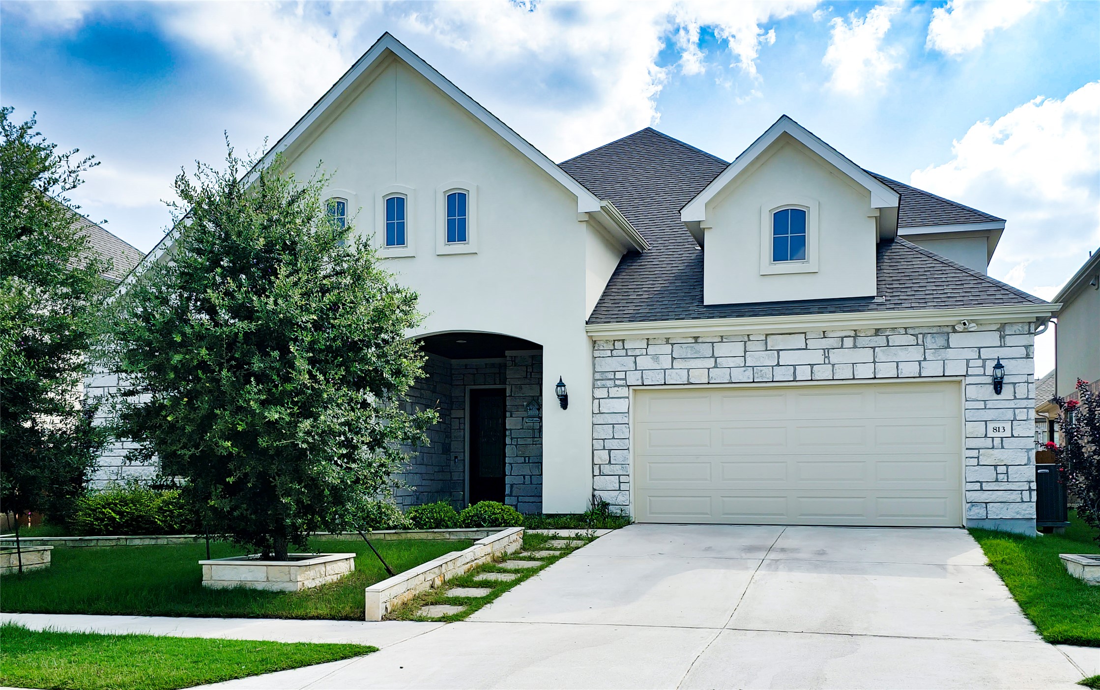Modern home with a garage, elegant white stone accents, and inviting landscaping.