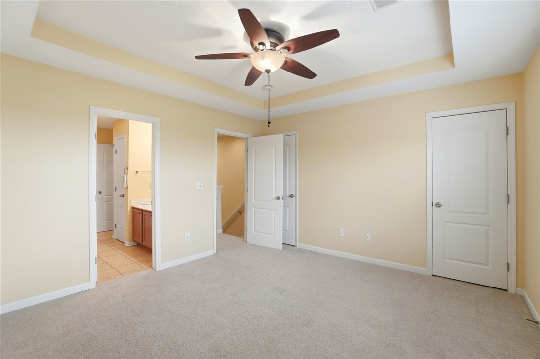 4324 Straight Arrow Road Dayton, OH 45430 - Photo 24 of 40 This spacious bedroom features a ceiling fan, soft carpeting, and a tray ceiling, with an adjacent bathroom visible.
