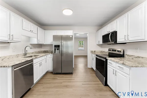 a kitchen with stainless steel appliances granite countertop white cabinets a sink a stove a refrigerator and a microwave