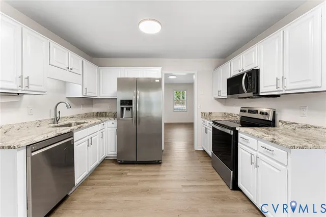 a kitchen with stainless steel appliances granite countertop white cabinets a sink a stove a refrigerator and a microwave