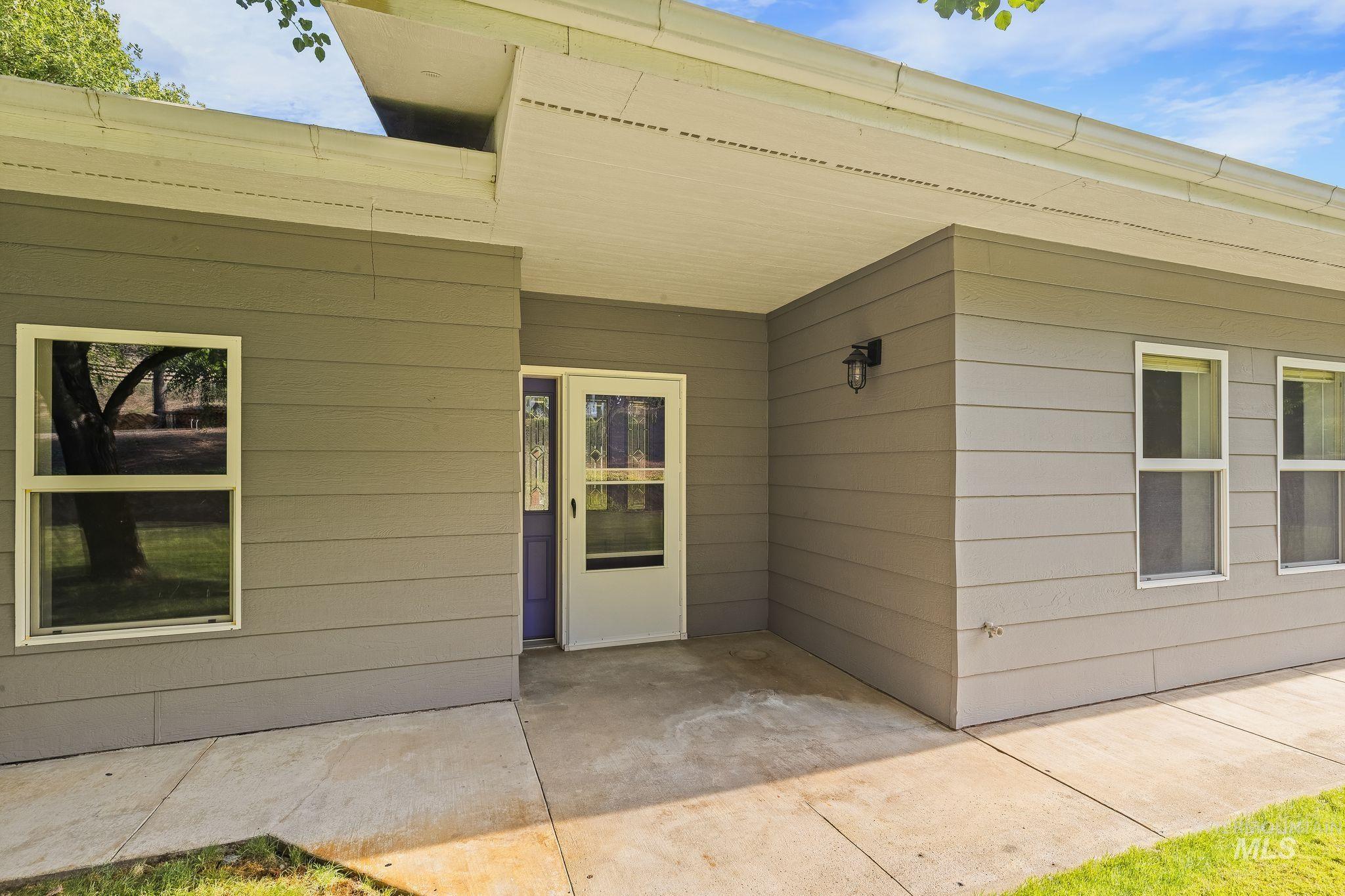 1091 Cedar Ridge Road Kendrick, ID 83537 - Photo 6 of 48 Exterior featuring gray siding, a covered concrete patio, white-framed windows, and a purple entry door with a white screen door