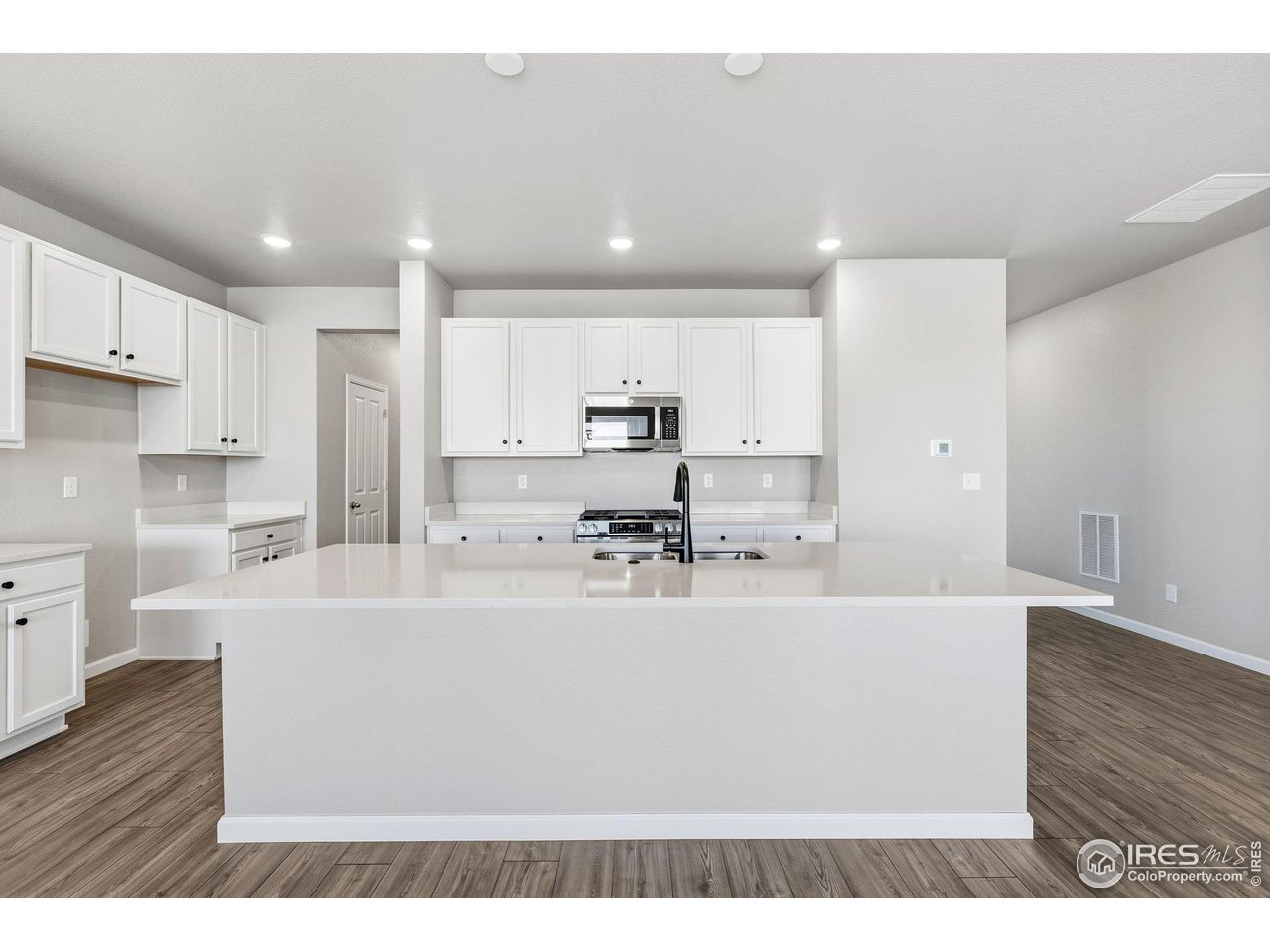 6793 Utica Court Firestone, CO 80504 - Photo 6 of 26 a large white kitchen with kitchen island a sink a stove a refrigerator and white cabinets