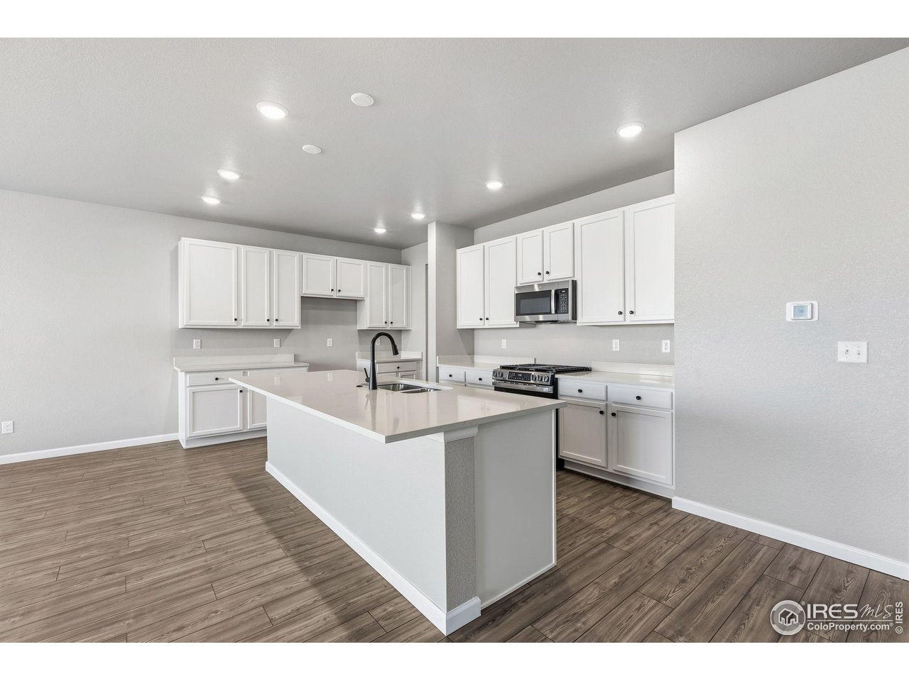 6793 Utica Court Firestone, CO 80504 - Photo 7 of 26 a large white kitchen with stainless steel appliances granite countertop a stove a sink a refrigerator and white cabinets with wooden floor