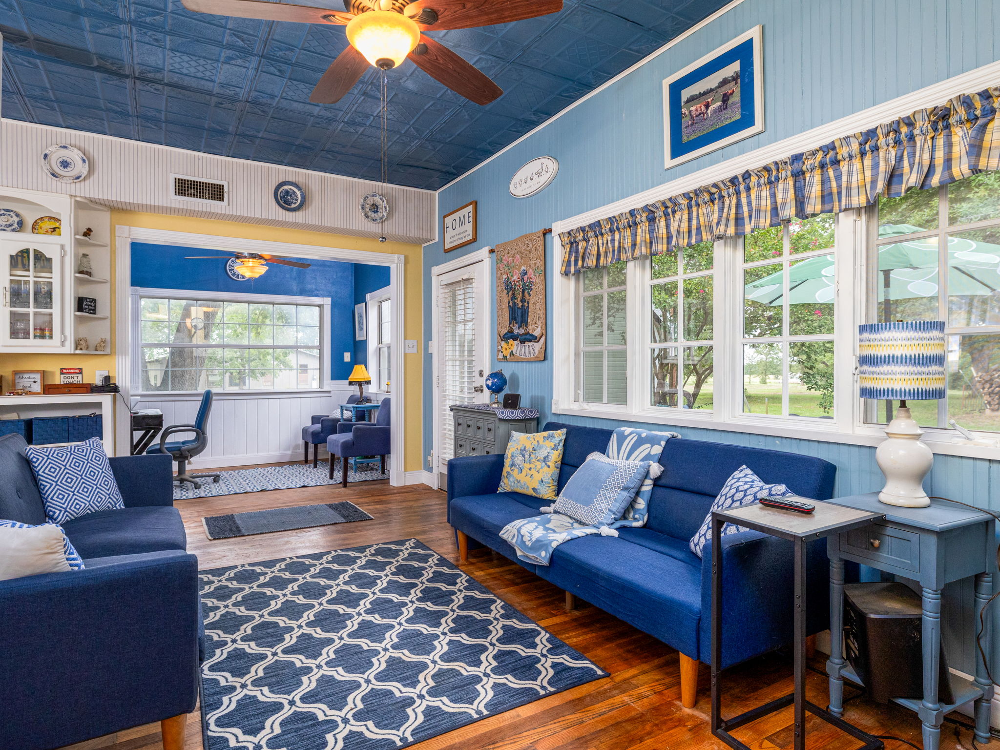 1065 Private Road 7041 Elgin, TX 78621 - Photo 8 of 38 Living area from another angle reveals the attached office space, framed by large windows that flood the room with natural light. Beautiful vintage tin ceiling and the wall detailing add character and depth, creating an inviting and functional space