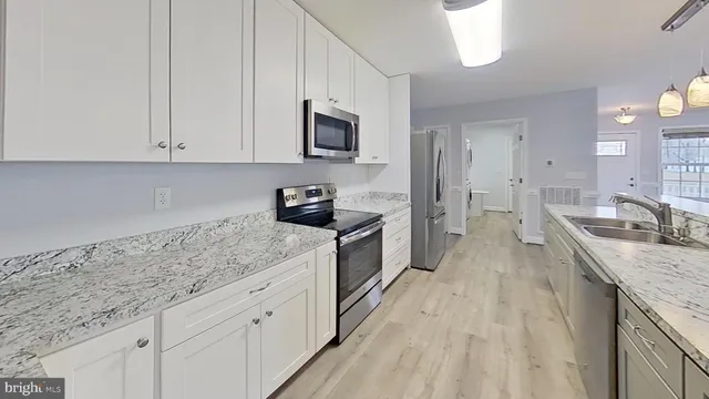 a kitchen with granite countertop a sink dishwasher stove and white cabinets with wooden floor