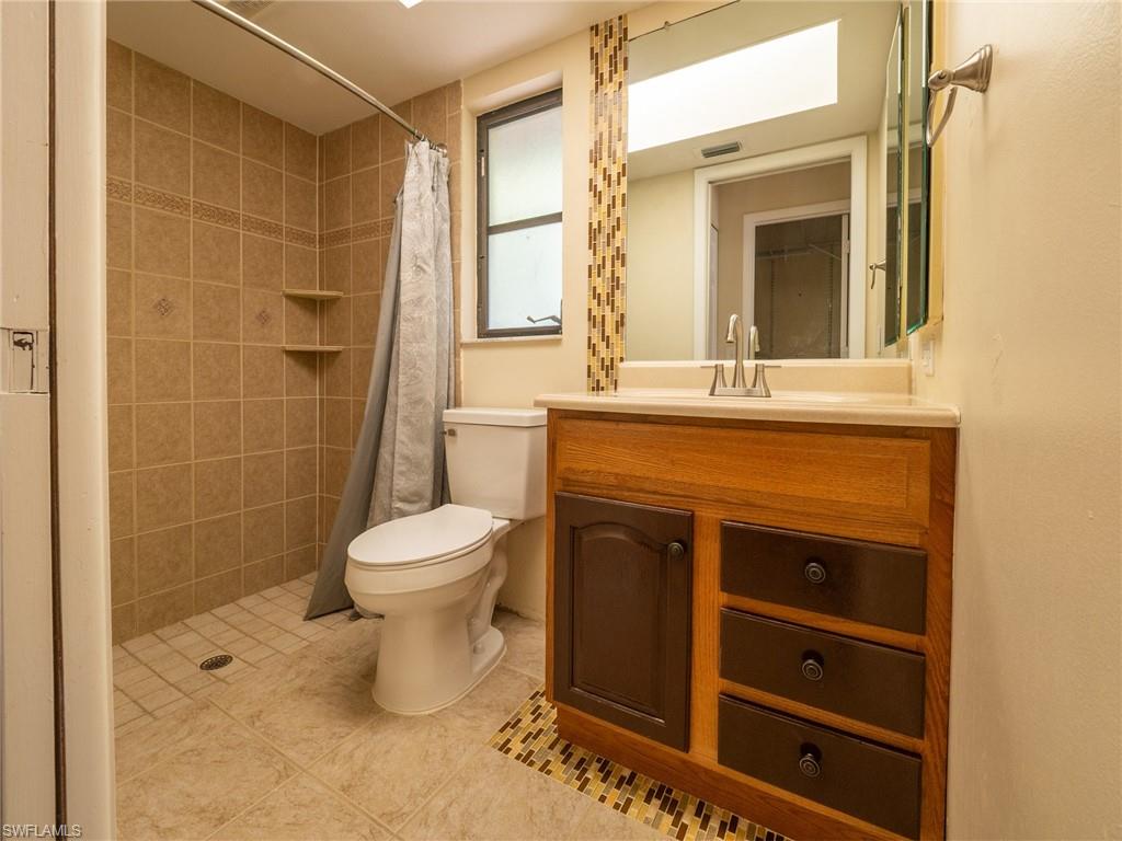18414 Tulip Road Fort Myers, FL 33967 - Photo 22 of 37 Bathroom featuring a walk-in shower with tile surround, a single vanity with a light wood-tone cabinet and contrasting drawer fronts, a solid surface countertop, and a built-in window