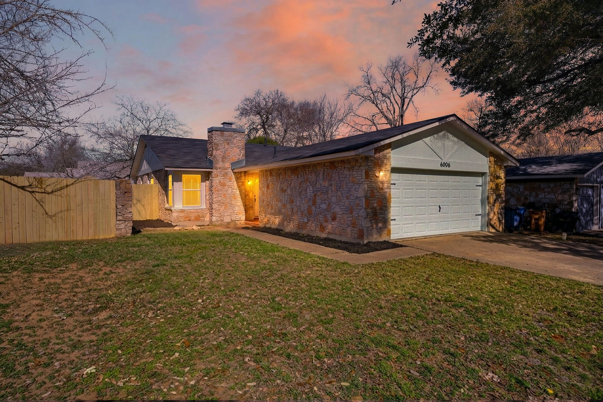 Mid-century inspired home with a chimney, stone siding, a garage, and driveway