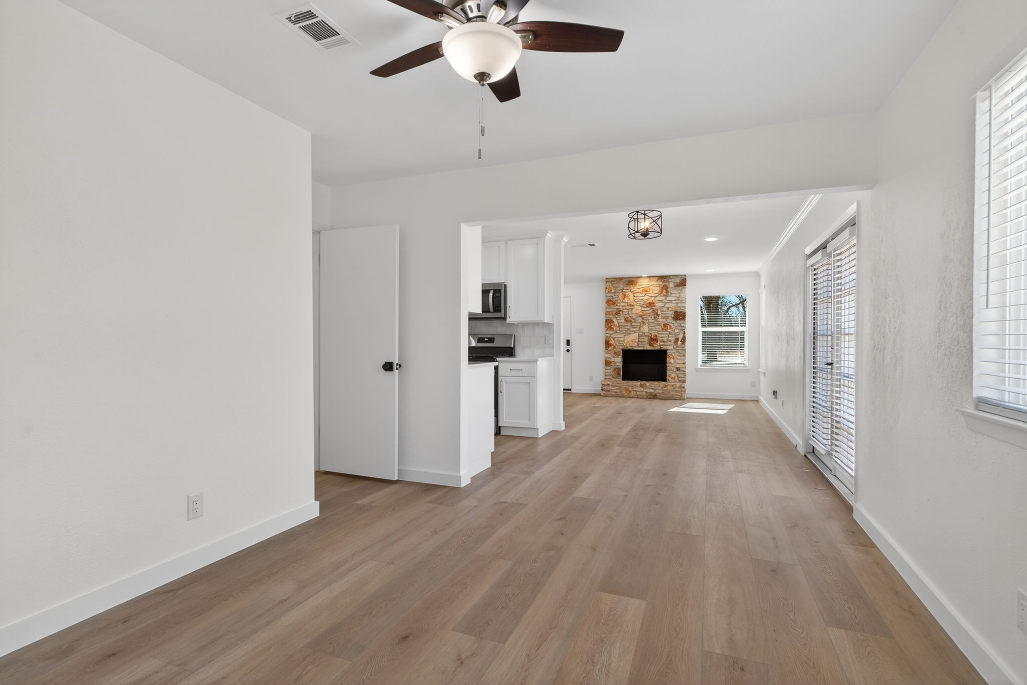 8400 Seminary Ridge Drive Austin, TX 78745 - Photo 11 of 37 Unfurnished living room with a ceiling fan, a stone fireplace, and light wood finished floors