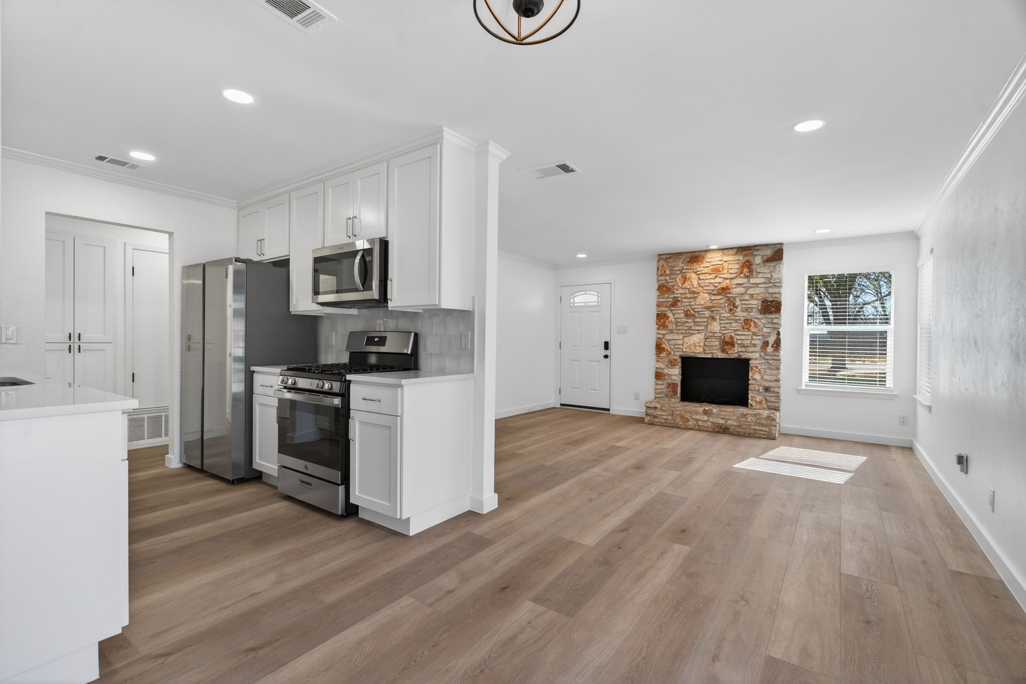 8400 Seminary Ridge Drive Austin, TX 78745 - Photo 12 of 37 Kitchen featuring stainless steel appliances, white cabinetry, ornamental molding, light wood-style flooring, and a stone fireplace