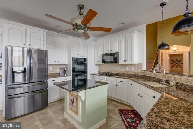 a kitchen with stainless steel appliances granite countertop a refrigerator a stove a sink and white cabinets with wooden floor