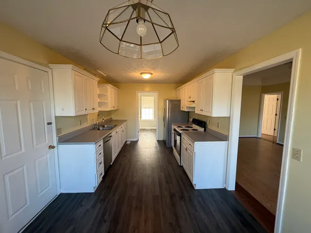 a kitchen with stainless steel appliances granite countertop a refrigerator a stove top oven a sink dishwasher and white cabinets with wooden floor