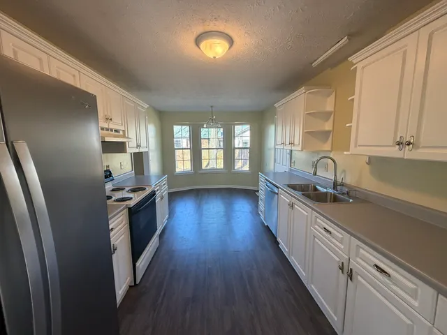 a large kitchen with stainless steel appliances a stove a refrigerator a sink dishwasher and wooden floor