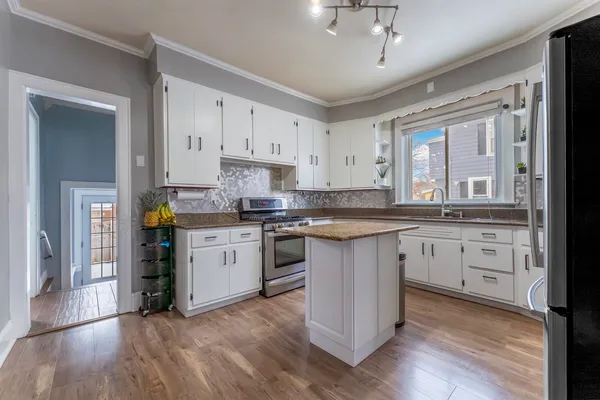 a kitchen with granite countertop a refrigerator a stove a sink and white cabinets with wooden floor