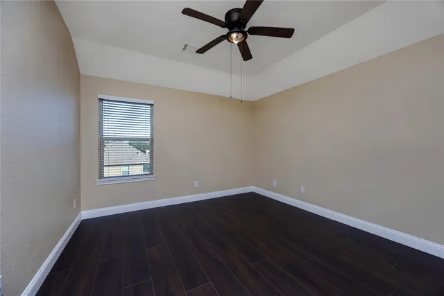 an empty room with wooden floor ceiling fan and windows