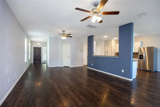 a view of an empty room with wooden floor and a ceiling fan