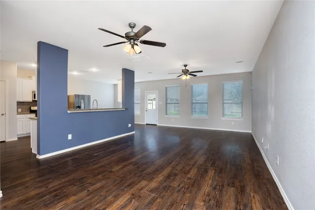 a view of an empty room with wooden floor and a ceiling fan