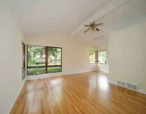 an empty room with wooden floor fan and windows