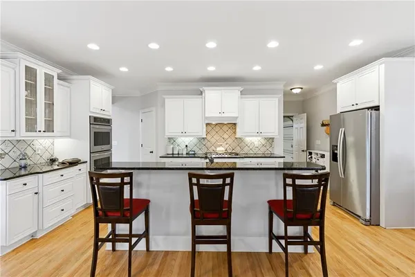 a kitchen with granite countertop white cabinets refrigerator and chairs