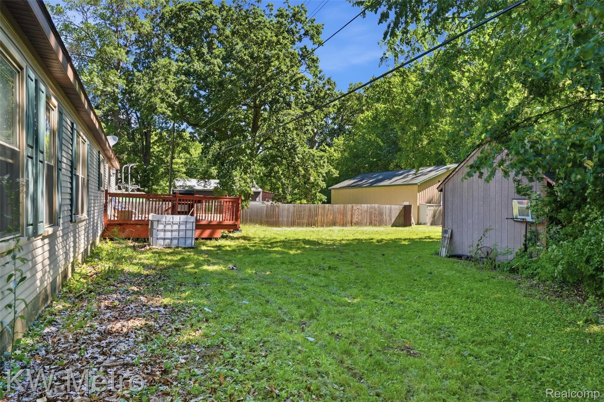 22733 Sumpter Road Belleville, MI 48111 - Photo 33 of 52 Expansive grassy lawn with a red-stained wood deck, a wood-paneled utility shed, and a privacy fence