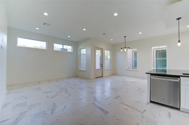 a view of an empty room with kitchen and window
