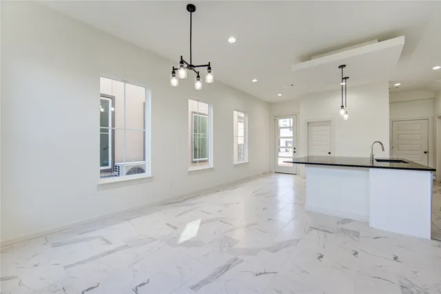 a large white kitchen with granite countertop a stove a sink a refrigerator and white cabinets with wooden floor