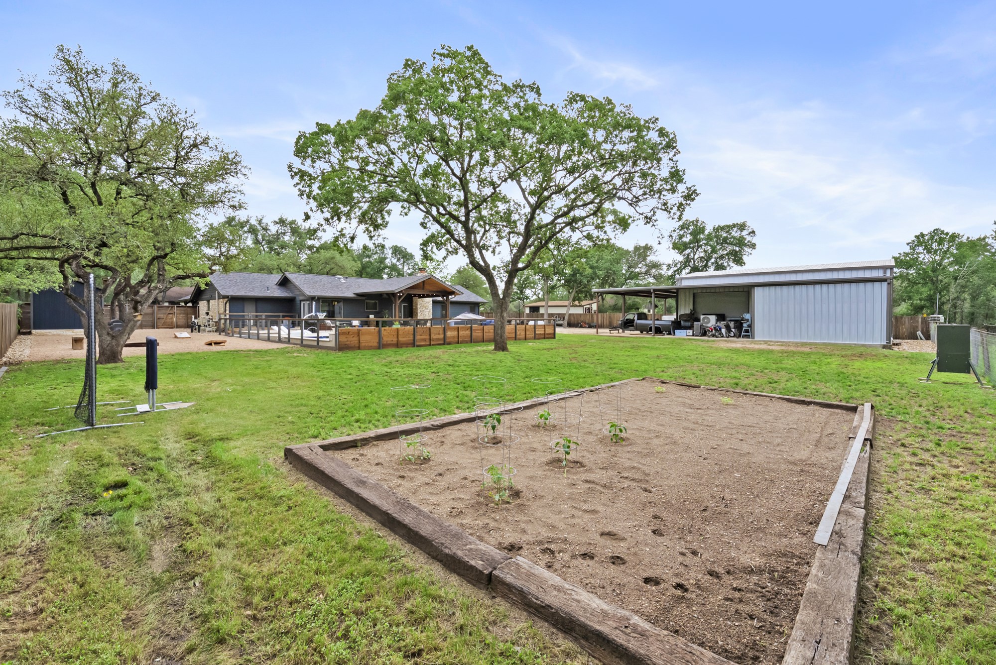2802 Robin Road Manchaca, TX 78652 - Photo 23 of 40 Expansive backyard featuring a large raised garden bed, mature trees, and a spacious metal outbuilding with a covered open bay