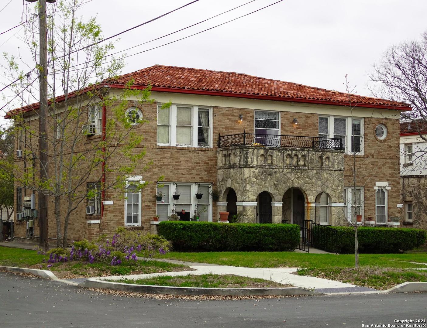 a view of a brick house with a yard plants and large trees