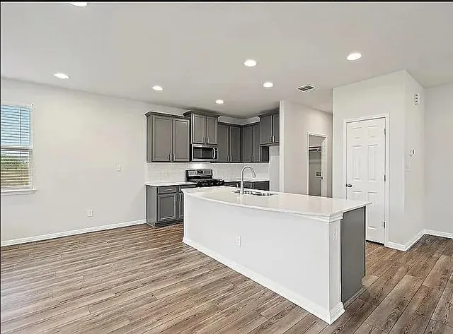 a large white kitchen with wooden floor and stainless steel appliances