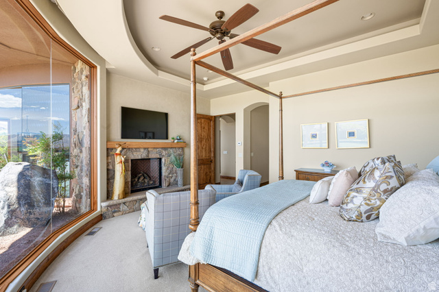 2331 West Entrada Trail, Unit 61 St. George, UT 84770 - Photo 26 of 69 Curved window wall, stone-faced fireplace with wood mantle, tray ceiling, recessed lighting, and a ceiling fan