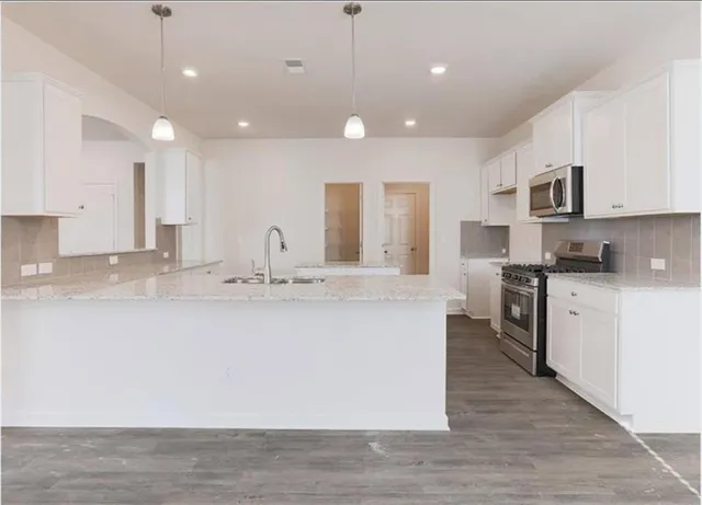a large kitchen with granite countertop a large counter top a sink stainless steel appliances and cabinets