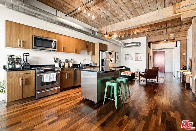 a kitchen with stainless steel appliances granite countertop a stove a refrigerator a kitchen island a dining table and chairs with wooden floor